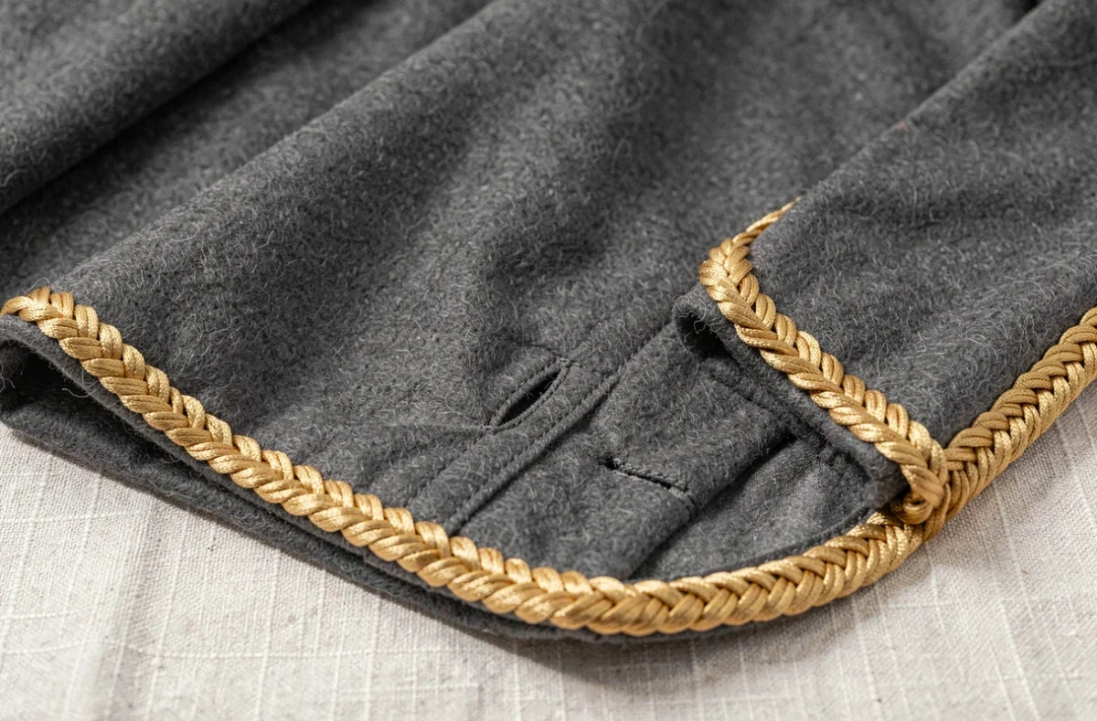 Détail macro d'un burnous gris anthracite haut de gamme avec passementerie dorée, sfifa et broderies à la main